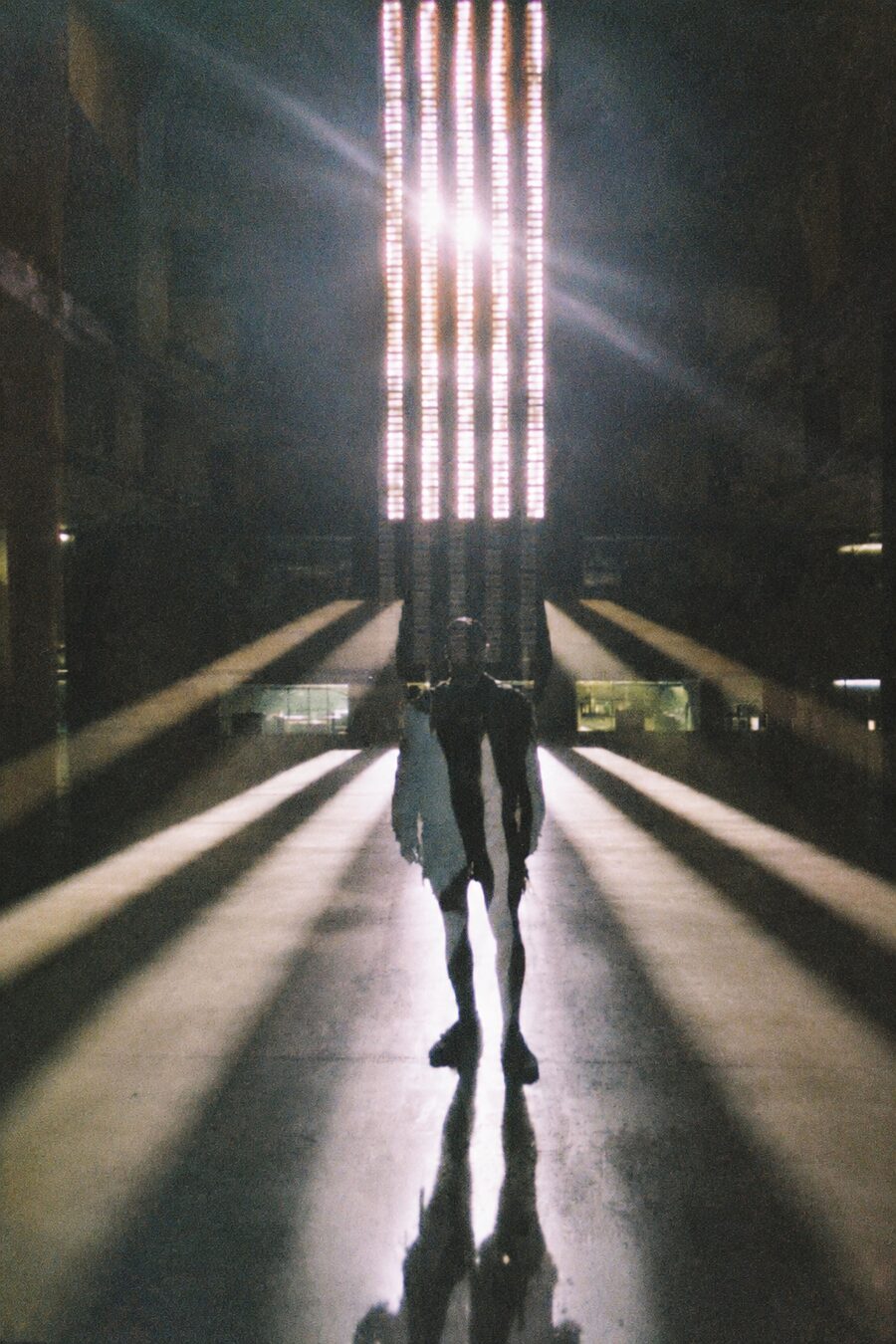 adán, backlit, standing in a long corridor of light